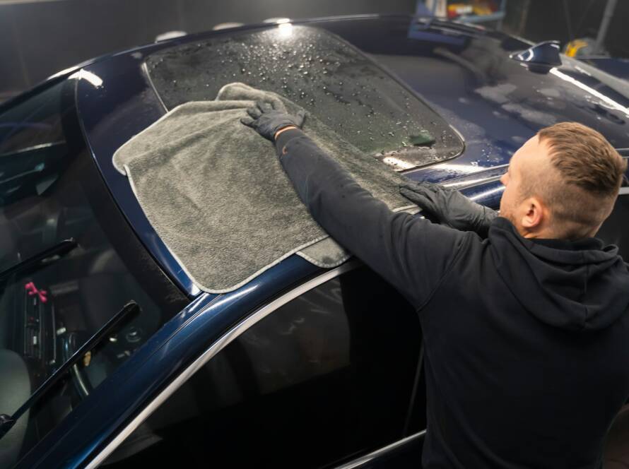 Car wash worker wipes the car after washing with microfiber towel. Professional car wash